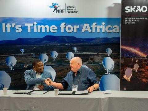 A picture of Prof. Phil Diamond, Director-General of the SKAO, and Prof. Thebe Rodney Medupe, President of AfAS, shaking hands while sitting at a table. Behind them on the wall is written “It’s time for Africa” with logo’s of SARAO, SKAO and AfAS.