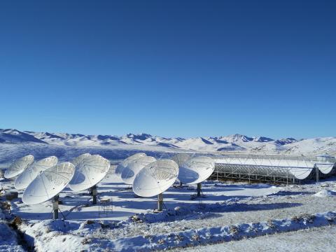 Nine telescope dishes and three open cylindrical telescopes in a snowy mountainous landscape under clear blue skies. 