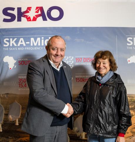 A man and woman shaking hands in front of a banner with the logo of SKAO.