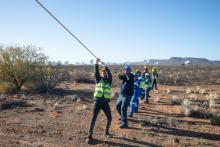 Team members pulling on a rope, with MeerKAT radio telescope in the background.